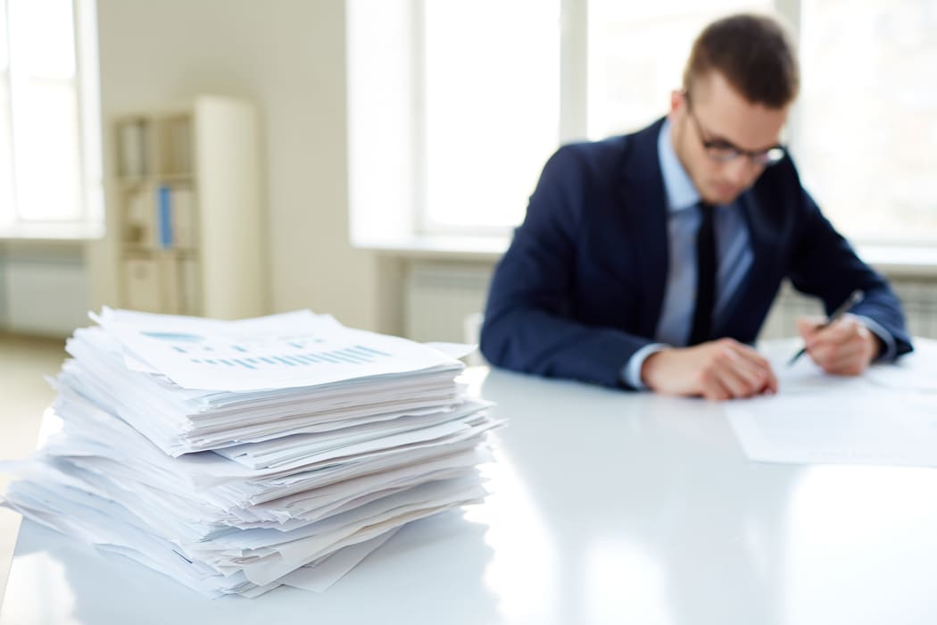 Hombre de negocios trabajando en papeleo con una gran pila de documentos al lado.